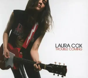 Trouble Coming de Laura Cox, 2025, Laura, Guitare rouge à la main, tout de noir vêtu, sur fond blanc de la pochette