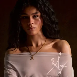 Ama Lou livre AMA, en 2026, pochette de l'album AMA, Ama Lou, photo en buste dans un crop mousseline beige, légèrement translucide, dur fond sombre.